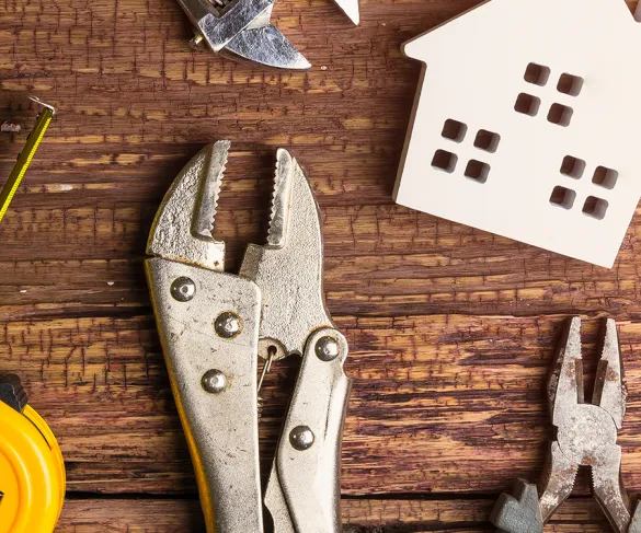 Metal pliers, tape measure, caliper, and wooden house model on a wooden surface.