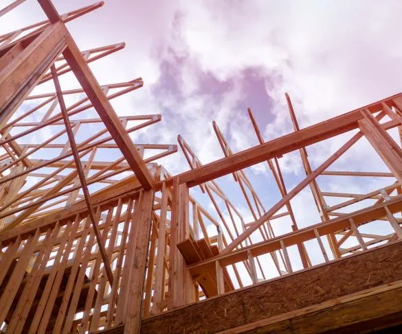 Wooden framing of a building under construction against a cloudy sky, showcasing exposed beams and support structures.