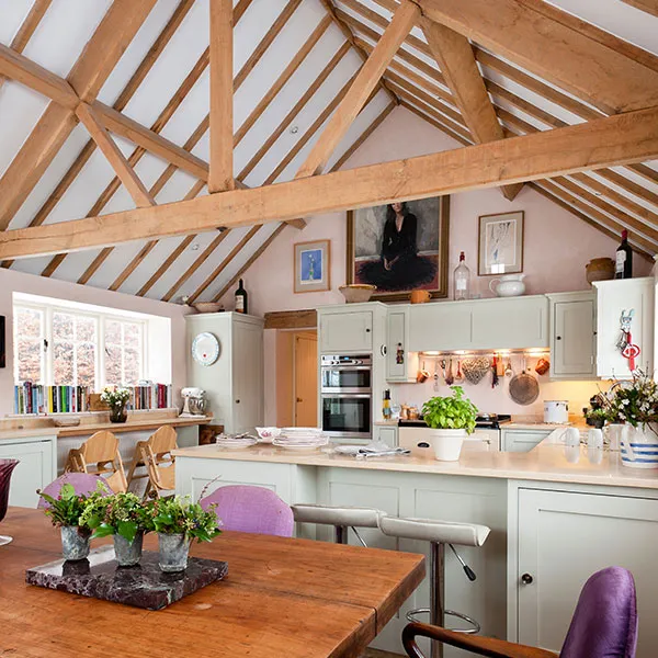 Spacious kitchen with exposed wood beams, a wooden dining table, light cabinets, modern appliances, and various artworks on the walls.