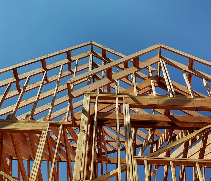 Wooden framework of a house under construction against a clear blue sky.