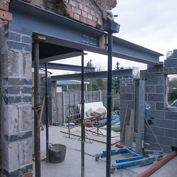 Partially constructed building with exposed steel beams, brick walls, scaffolding, and various construction materials around.