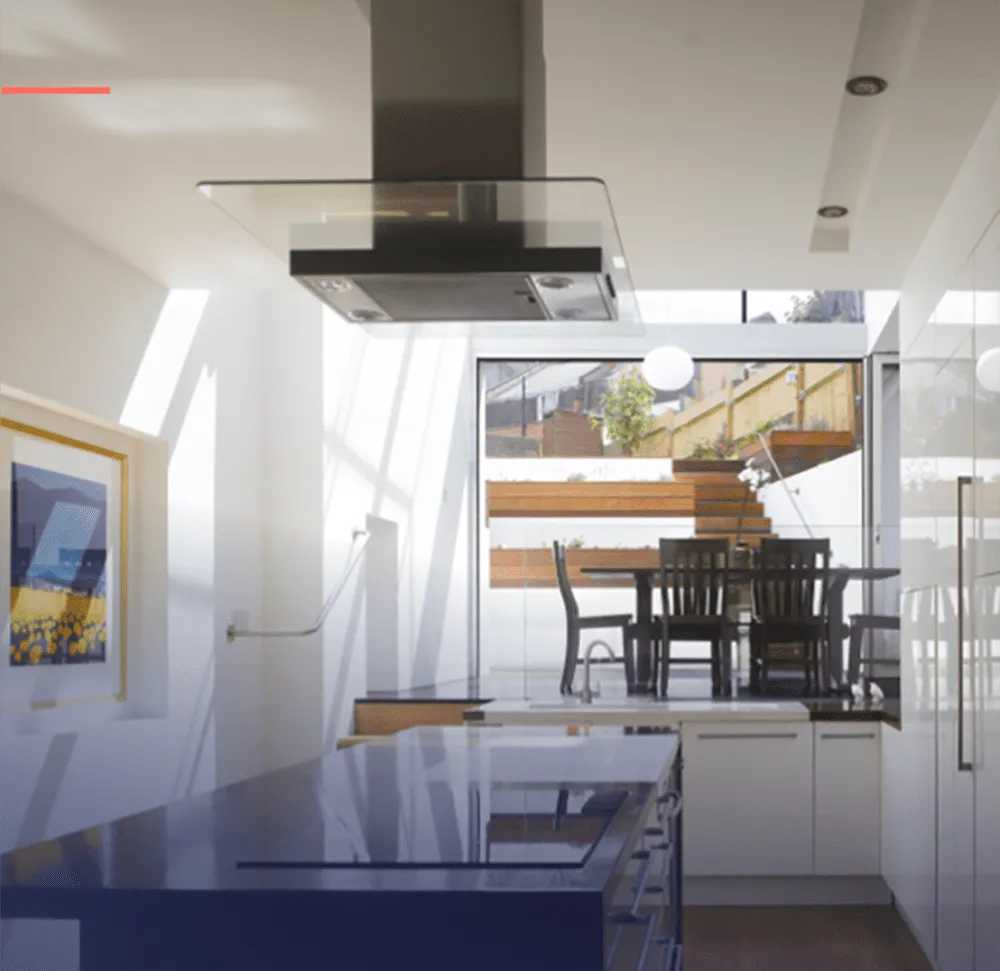 Modern kitchen interior with a sleek island, glass range hood, white cabinets, and a dining area with a large window view to the outside.