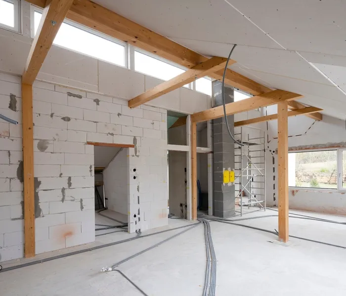 Interior of a building under construction, featuring wooden beams, exposed brick walls, and electrical wiring in progress.