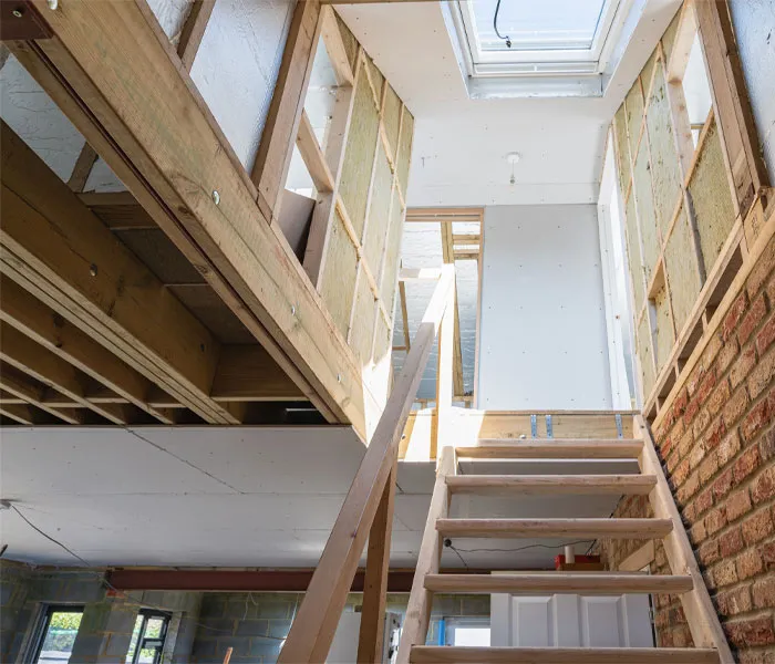 Interior view of a house under construction with exposed wooden framing and a partially built staircase leading to the upper level.