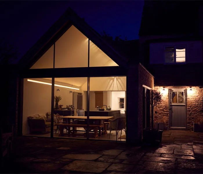 Night view of a modern house with large floor-to-ceiling windows, showcasing a lit interior with a living and dining area.