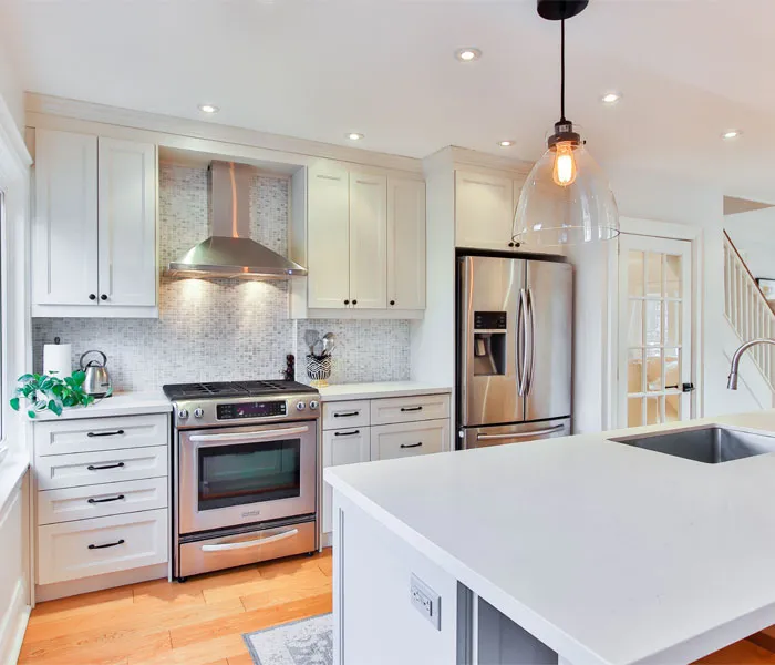 Modern kitchen with white cabinets, stainless steel appliances, a kitchen island with a sink, and a pendant light fixture.