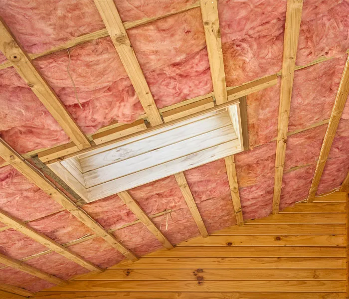 Unfinished wooden ceiling frame with pink insulation and a rectangular opening for a skylight in a room under construction.