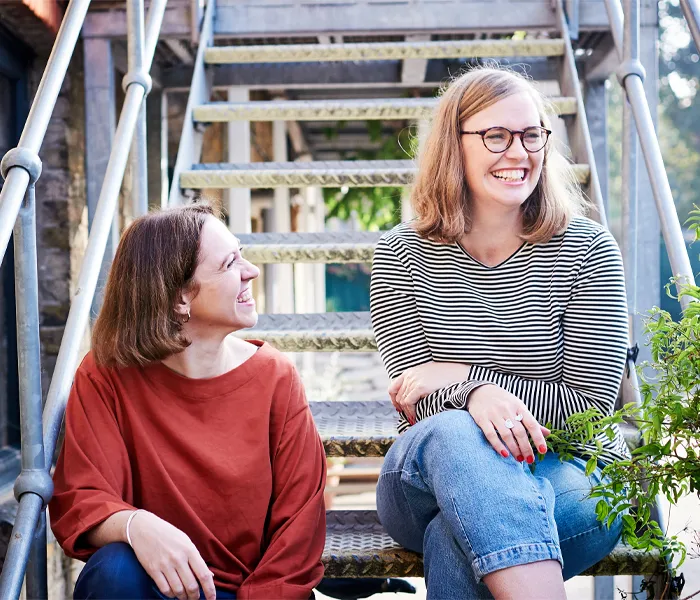 Two women seated on a staircase, engaged in conversation, with a warm and inviting atmosphere surrounding them.